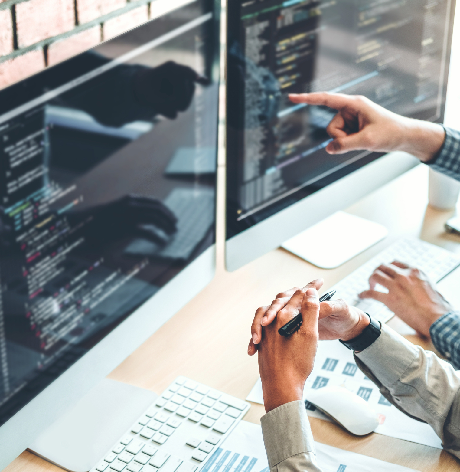 Two developers collaborating on code displayed on multiple computer monitors0