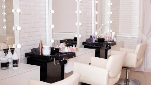 Modern beauty salon interior with white salon chairs and large vanity mirrors framed by lights against a white brick wall